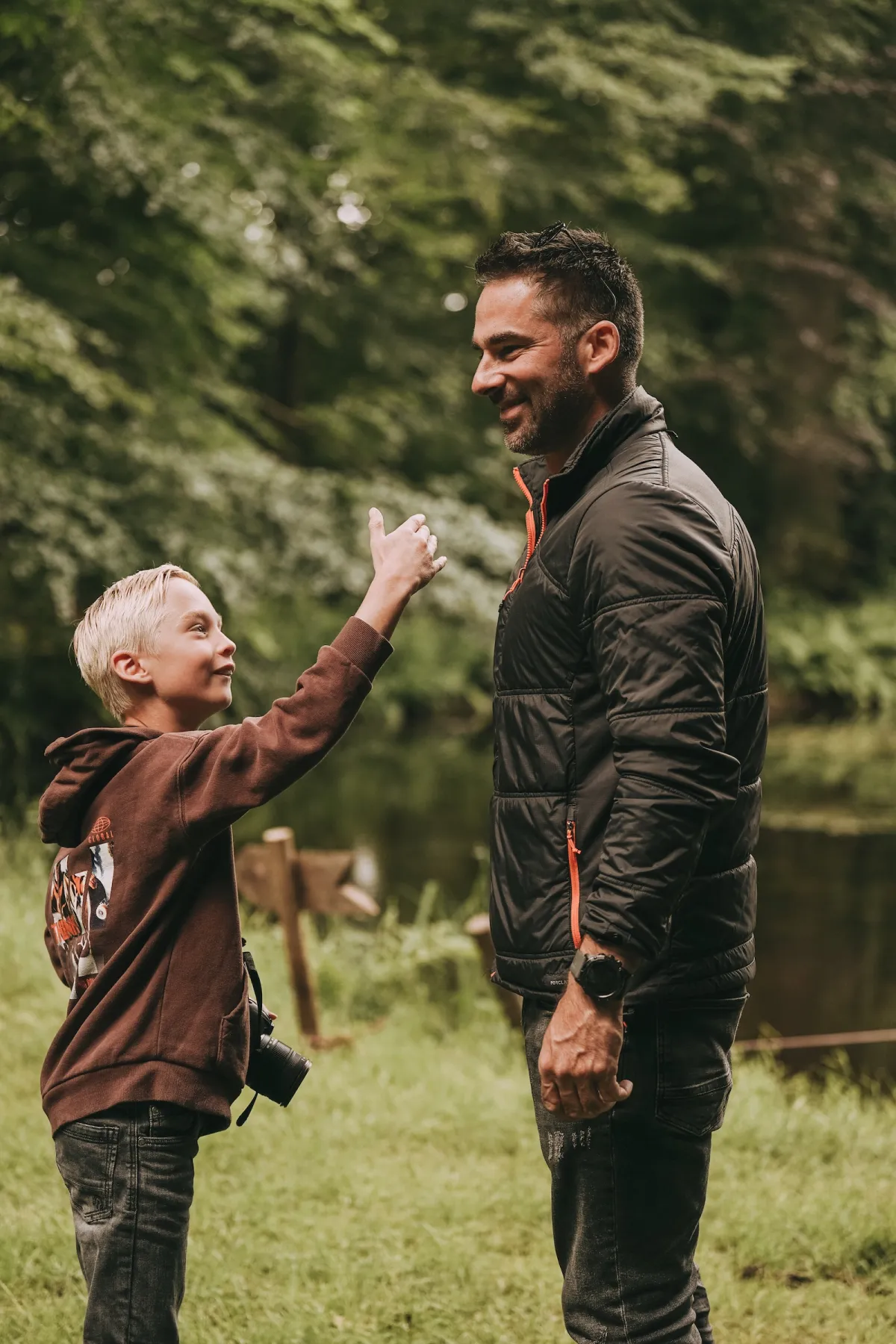 Begeleider geeft een lachende jongen met een spiegelreflexcamera om zijn nek een high five op een grasveld