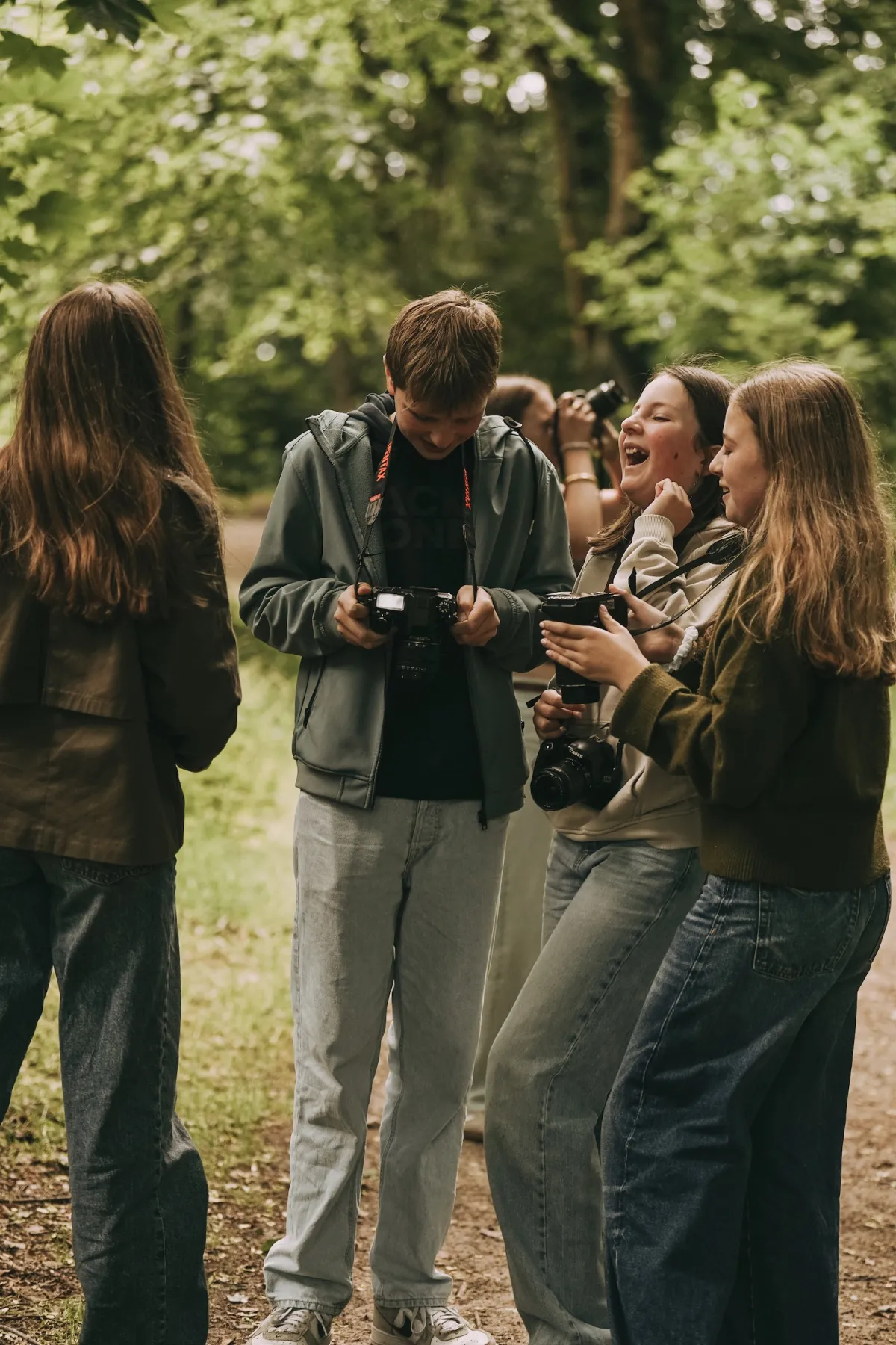 Groepje tieners staat dicht bij elkaar op een bospad met hun camera's in de hand en lacht om een gemaakte foto