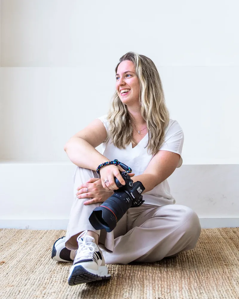 Sanne Jongstra zit lachend op de grond met een spiegelreflexcamera in haar handen