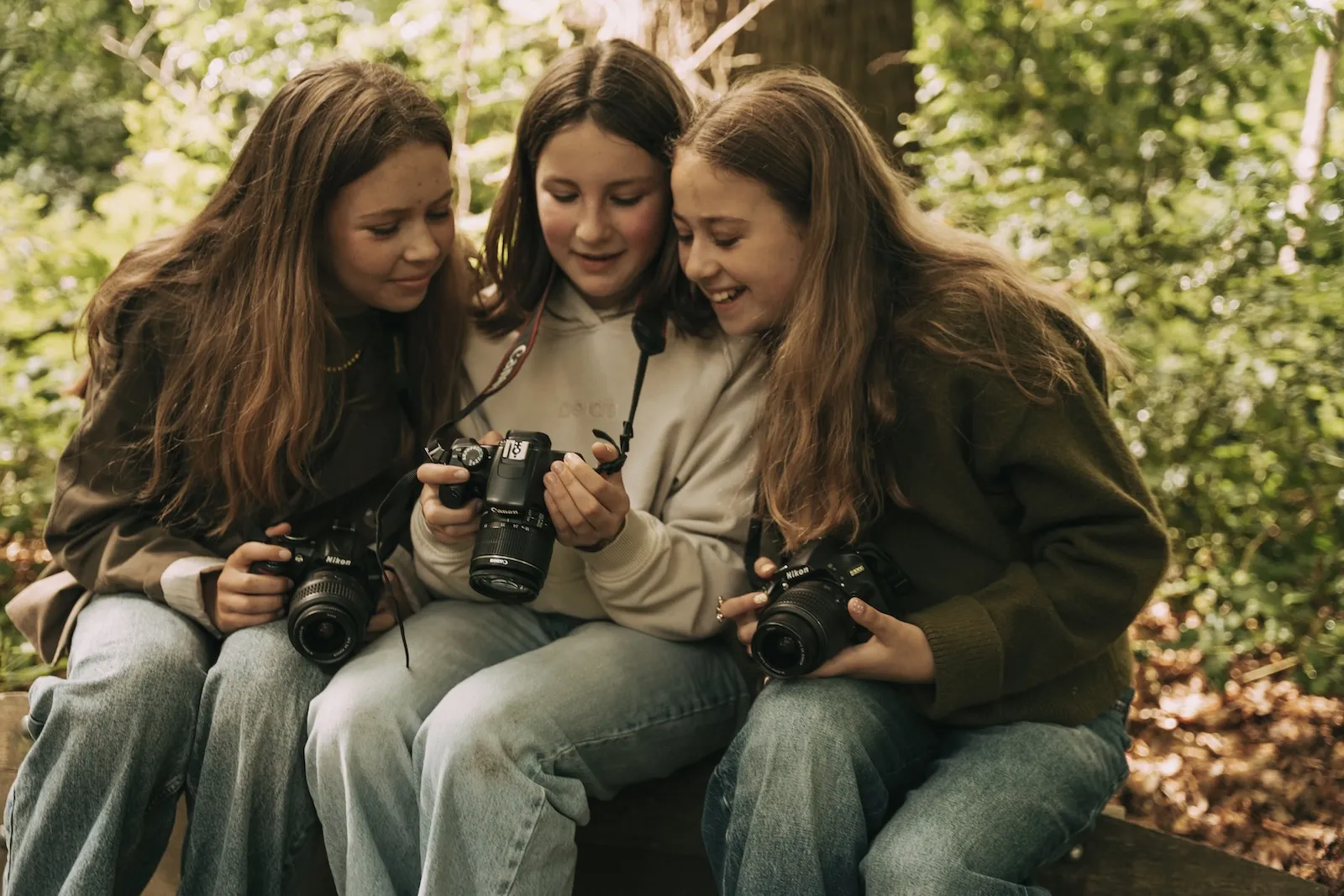 Drie tienermeisjes bekijken samen een foto op het schermpje van een Canon-camera, met twee Nikon-spiegelreflexcamera's op schoot