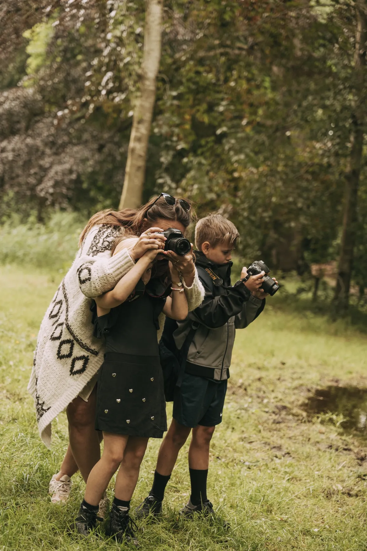 Twee kinderen en een begeleidster fotograferen dicht naast elkaar in het gras met hun Canon- en Nikon-camera's